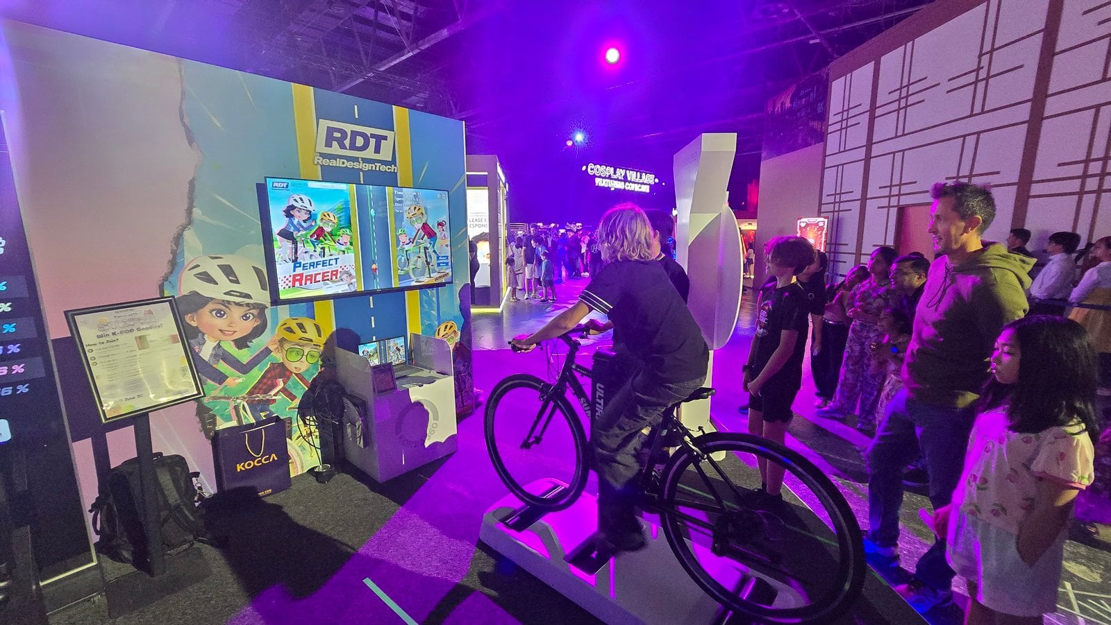 Stand de Ultiracer de RealDesignTech y Korea360 UAE en GameExpo 2026, Centro de Comercio Mundial de Dubái Un visitante pedalea en una bicicleta Ultiracer frente a la pantalla de Perfect Racer en el stand de RealDesignTech mientras el público observa