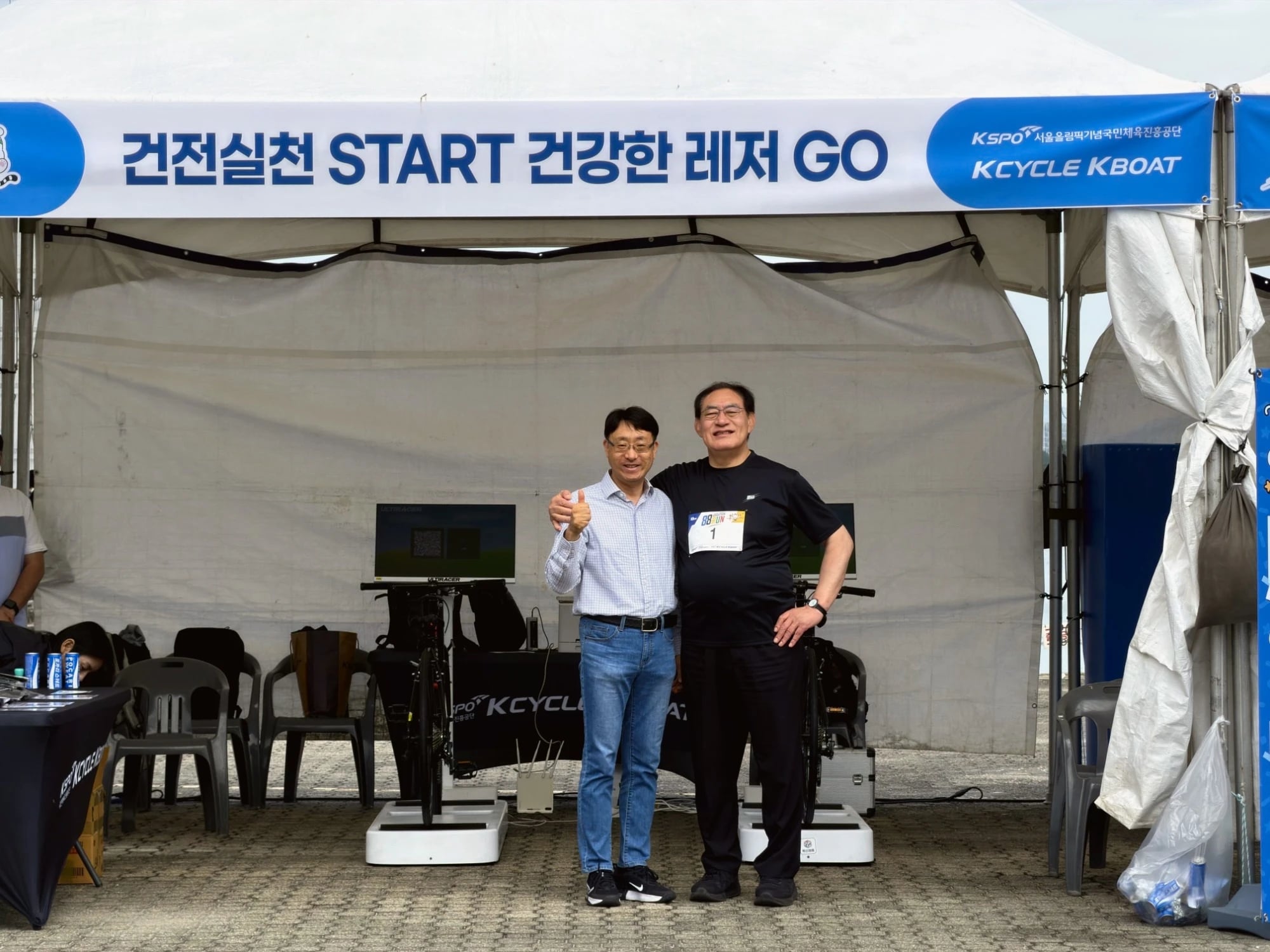 88RUN 부스의 하형주 이사장과 이중식 대표이사 KCYCLE KBOAT 부스 배너 아래 Ultiracer (얼티레이서) 자전거 두 대 앞에서 어깨동무를 한 두 남성. 오른쪽은 88RUN 1번 배번을 달았고 왼쪽은 엄지를 들어 보이는 모습