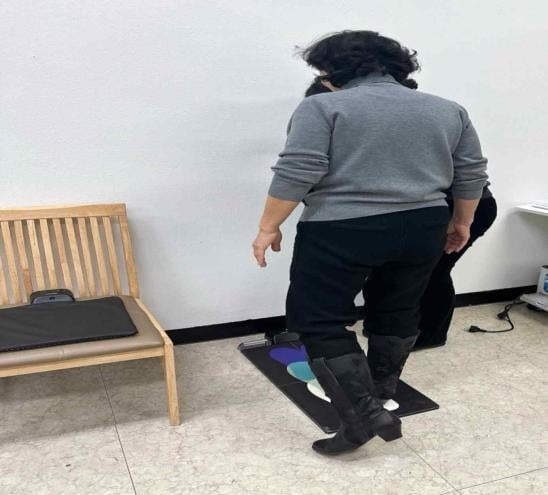An older woman seen from behind standing with her feet in position on a balance test mat