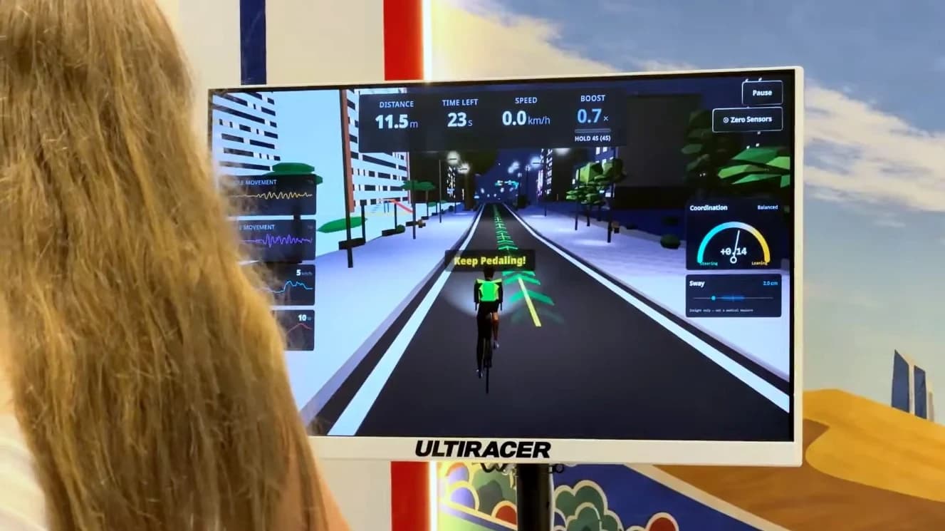 Modo Perfect Racer en el Ultiracer Kiosk Pantalla del Ultiracer Kiosk en modo Perfect Racer con distancia, velocidad, impulso, un indicador de coordinación y la lectura de balanceo mientras un ciclista recorre un circuito urbano