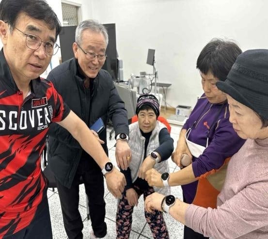 A group of older participants holding out their wrists to compare the heart rate readings on their smartwatches