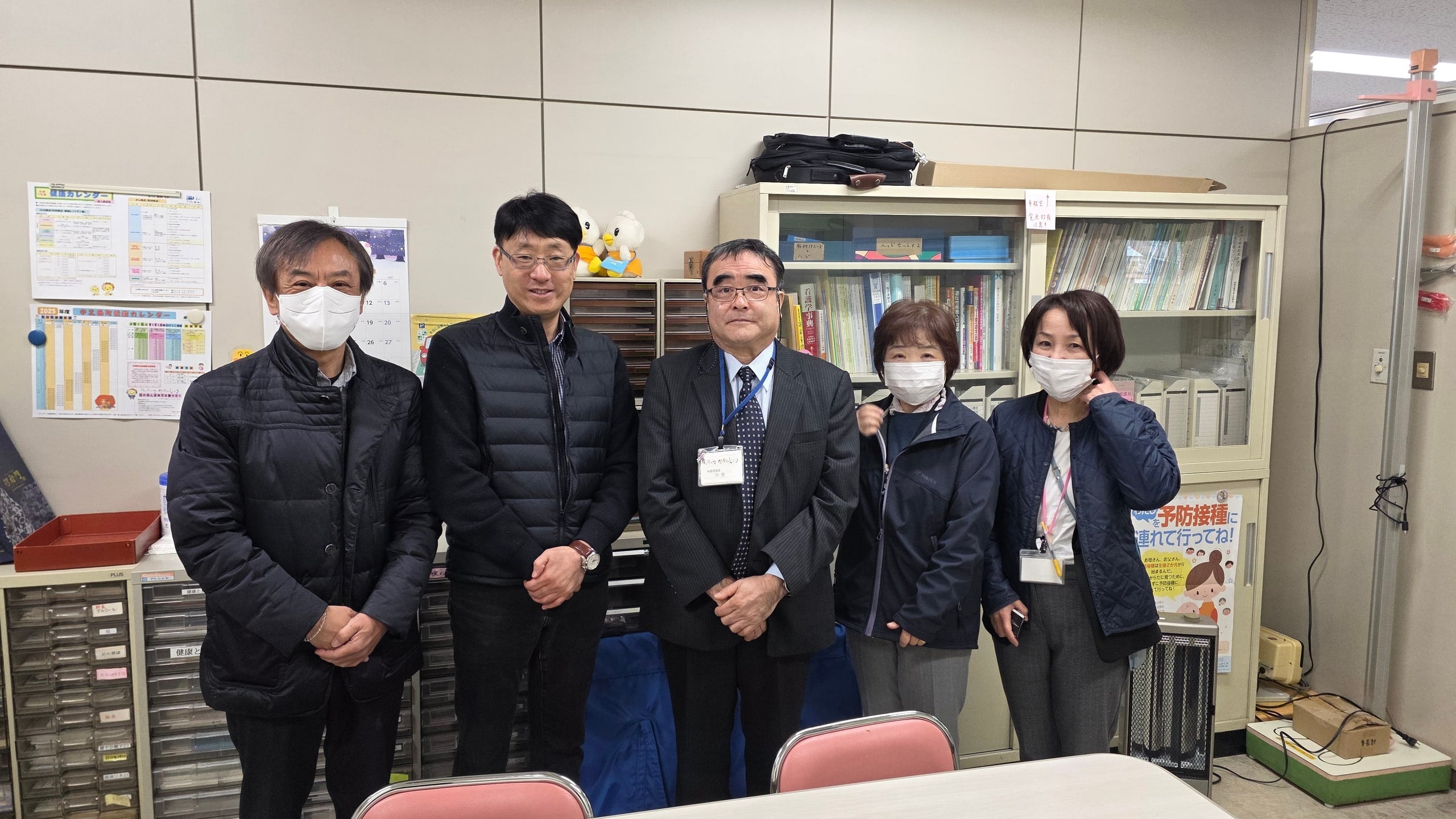 Meeting at Nakanojo Town Health Center Members of the Ultiracer team stand with staff in an office at Nakanojo Town Health Center, with health calendars and bookshelves behind them
