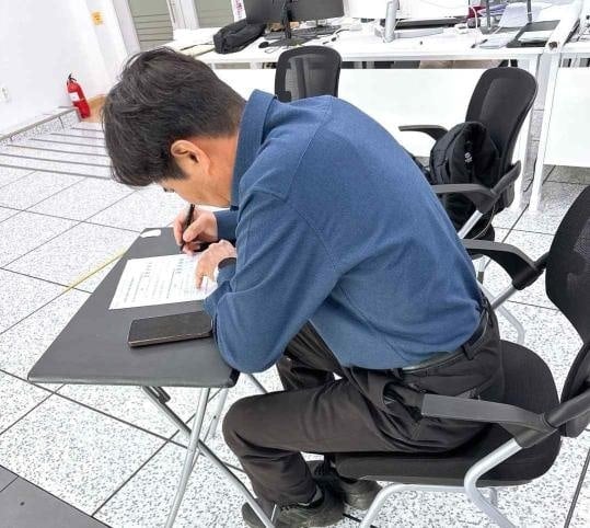 An older man seated at a small table filling in a paper questionnaire