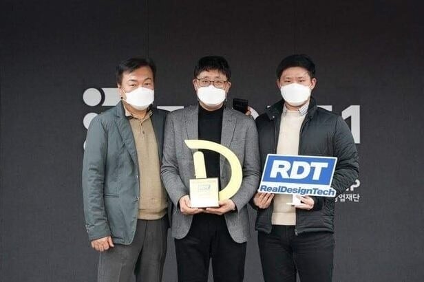 الفوز بـ D.DAY، 2021 ثلاثة رجال يرتدون الكمامات يحملون كأس D.DAY ولافتة RDT RealDesignTech على المسرح