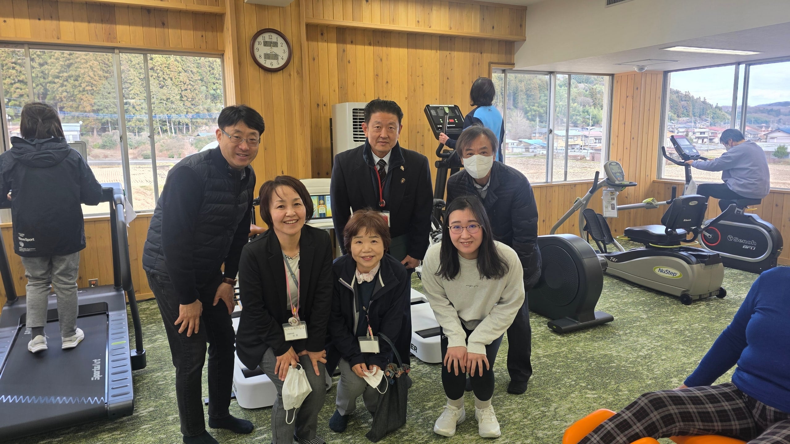 Installation day in Nakanojo The Ultiracer team and local staff smile for a group photo in a bright wood-panelled fitness room in Nakanojo, with treadmills and recumbent steppers behind them